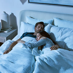 Young couple in pajamas lying asleep in bed with their arms around each other.