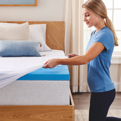 Young woman kneeling at the corner of the bed pulling the soft white slip cover over the revealed corner of premium foam