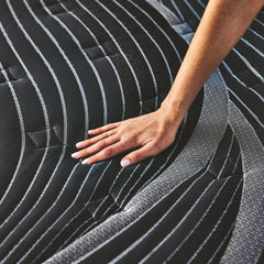 Woman's hand pressing down on the black and gray Noir Mattress cover to show its plush comfort
