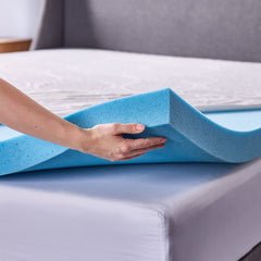 A closeup corner view of a woman’s hand holding up the gel memory foam layer, revealing how it is placed directly on top of a mattress.