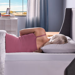 The young woman lies on her side in bed, showing how the ComfortLuxe Plus Topper gently supports her back and body with proper spinal alignment. 