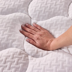 A woman’s hand presses down into the plush fiberfill cover of the topper, showing the luxurious softness and the rounded diamond pattern with wicker detailing. 