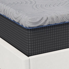 Close up corner view of the foam mattress base cover with a charcoal grid design below the light gray quilted top connected by royal blue stitching 