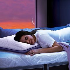 Young woman asleep lying on her stomach on the ComfortGrande Plus Mattress with her head resting on the ComfortGrande PIllow with early sunrise seen out the window