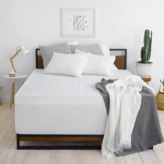 Front view of a bed with the Overnight Recovery Topper cover pulled completely over the mattress and set with white and gray pillows and throw blankets