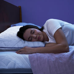 Young woman in pajamas lying on her side in bed with her head propped up on the Novaform ComfortGrande Plus Pillow and her hand resting next to the cover