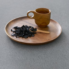 Wooden plate set with matching cup and spoon next to a pile of odor neutralizing charcoal resting on top of the gray SoFresh Topper cover