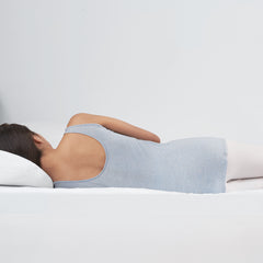 Young woman wearing pajamas lying in bed on her stomach propping her torso up against the foam topper and resting her head on her right arm